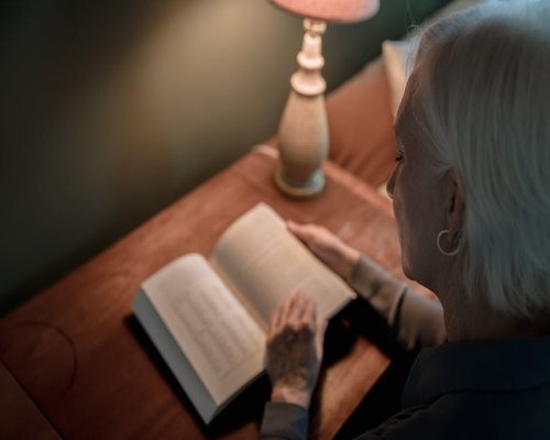 Person reading a book with a warm desk lamp at night